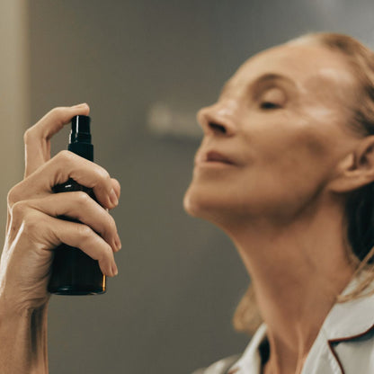 A guest holding a spray bottle of hydrating face mist, preparing to apply it to their face.