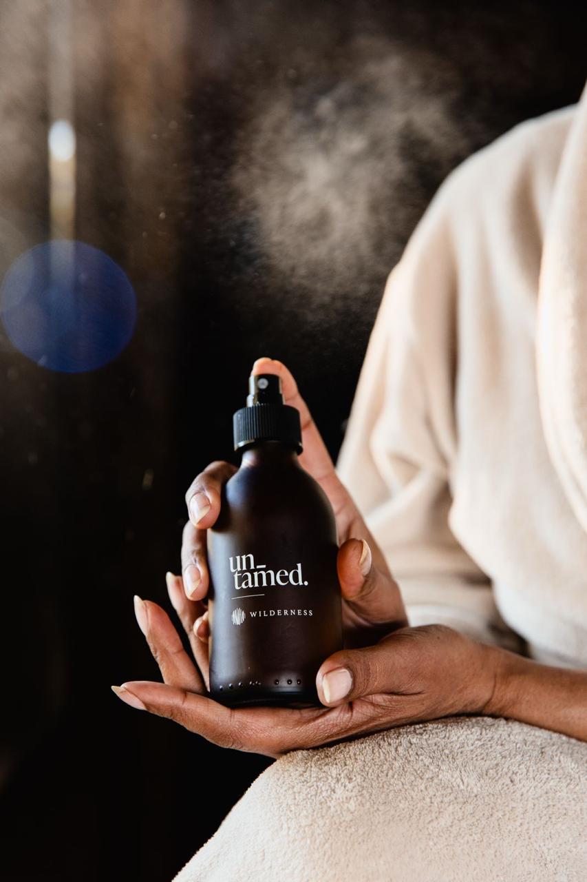 Person holding an amber bottle labeled 'untamed' with a blurred background